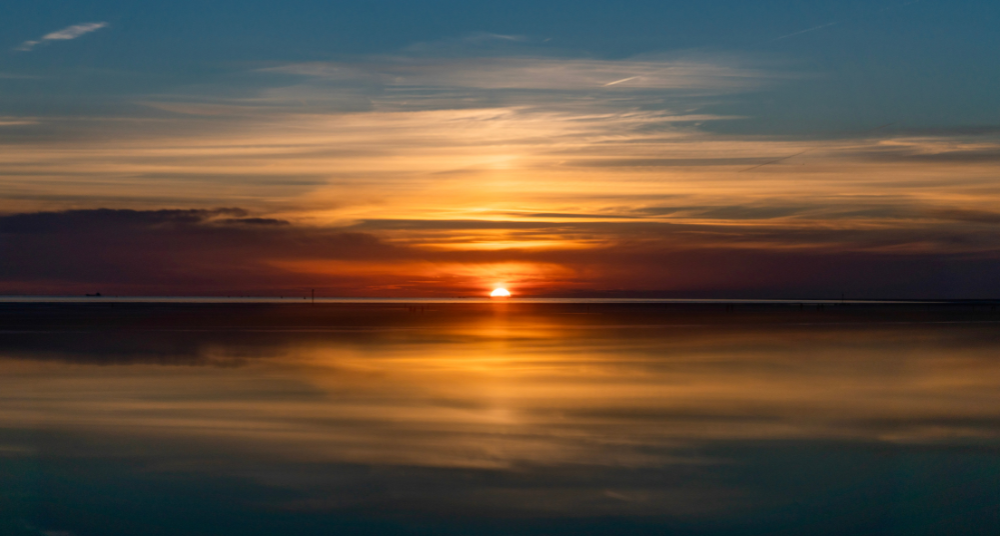 A dark, moody sunrise over the ocean representing the Winter Solstice and the return of longer, sunnier beach days.