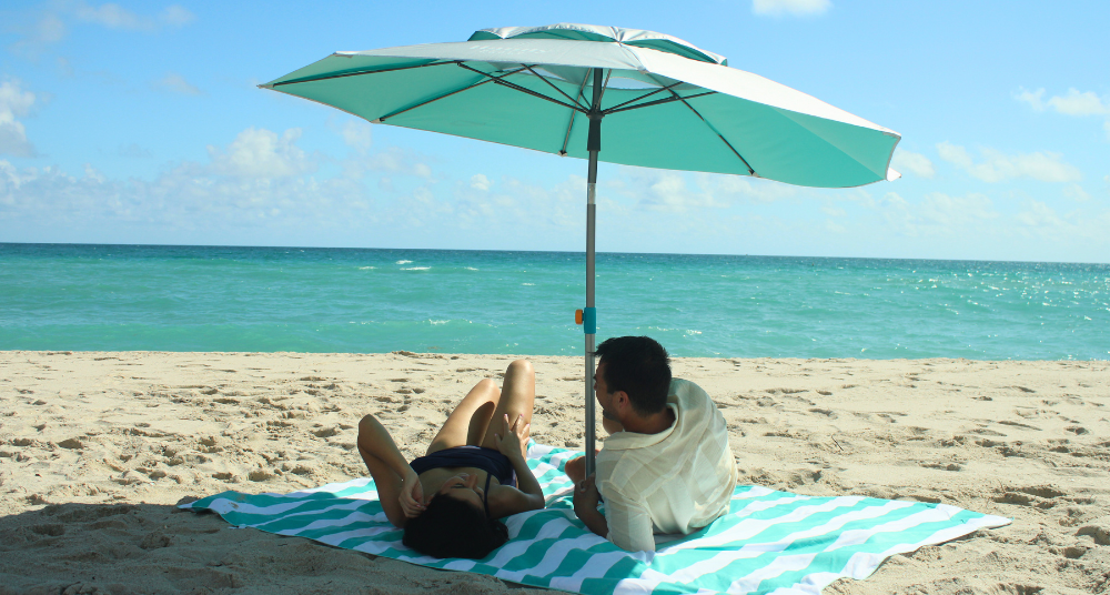 A tidy beach setup featuring a Handy Beach Umbrella anchored through the center slot of a sand-free Handy Beach Blanket, creating an organized "base camp" on the sand.
