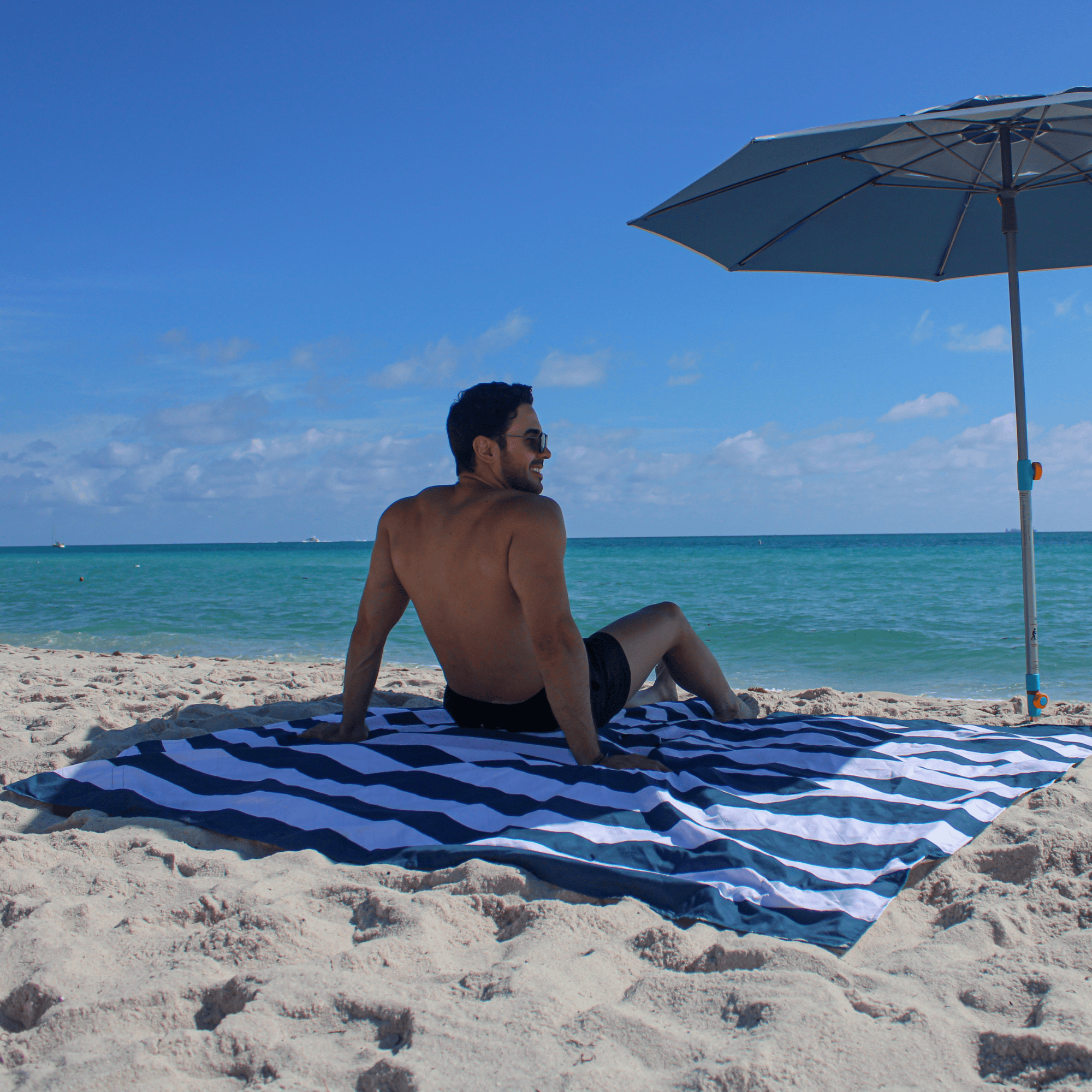 Man sitting on a sand-repellent beach blanket featuring a fully waterproof underside to block damp sand.