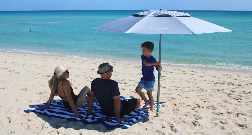 Family relaxing stress-free on a Handy Beach Blanket under a wind-safe Handy Beach Umbrella during a sunny spring break vacation.