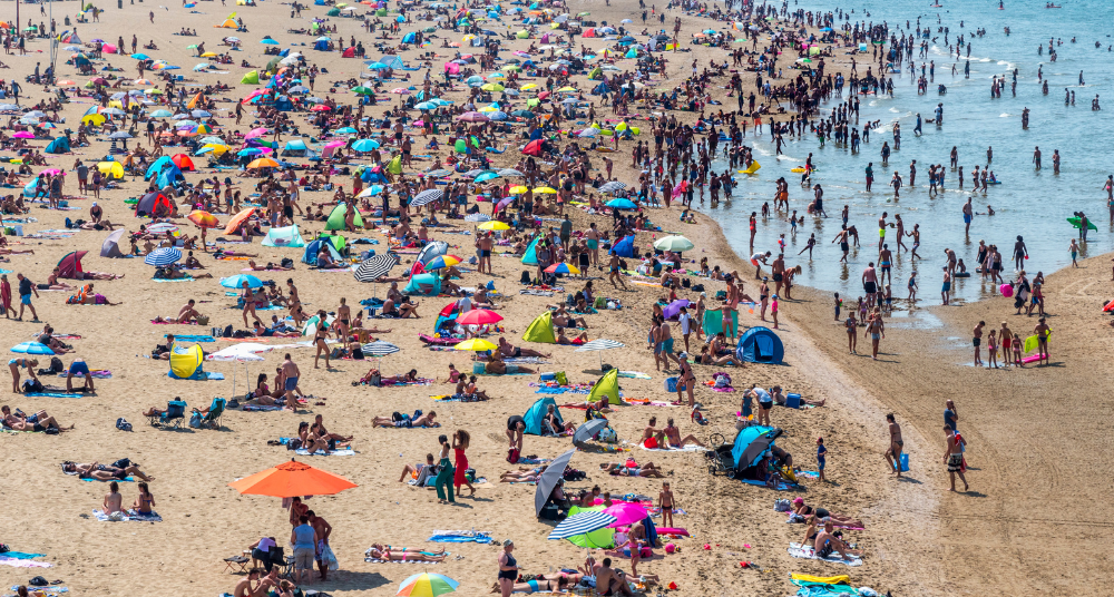 A heavily crowded sandy beach during spring break with overlapping towels, large tents, and beachgoers packed closely together.