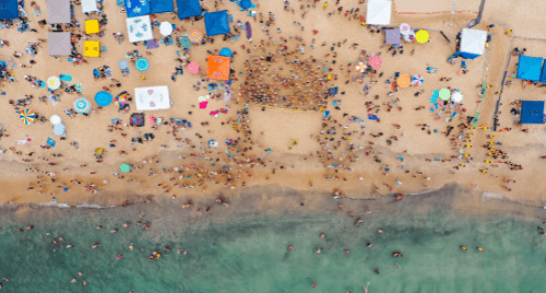 A crowded summer beach scene packed with large canopy tents and sprawling wind shades taking up massive amounts of sand space.
