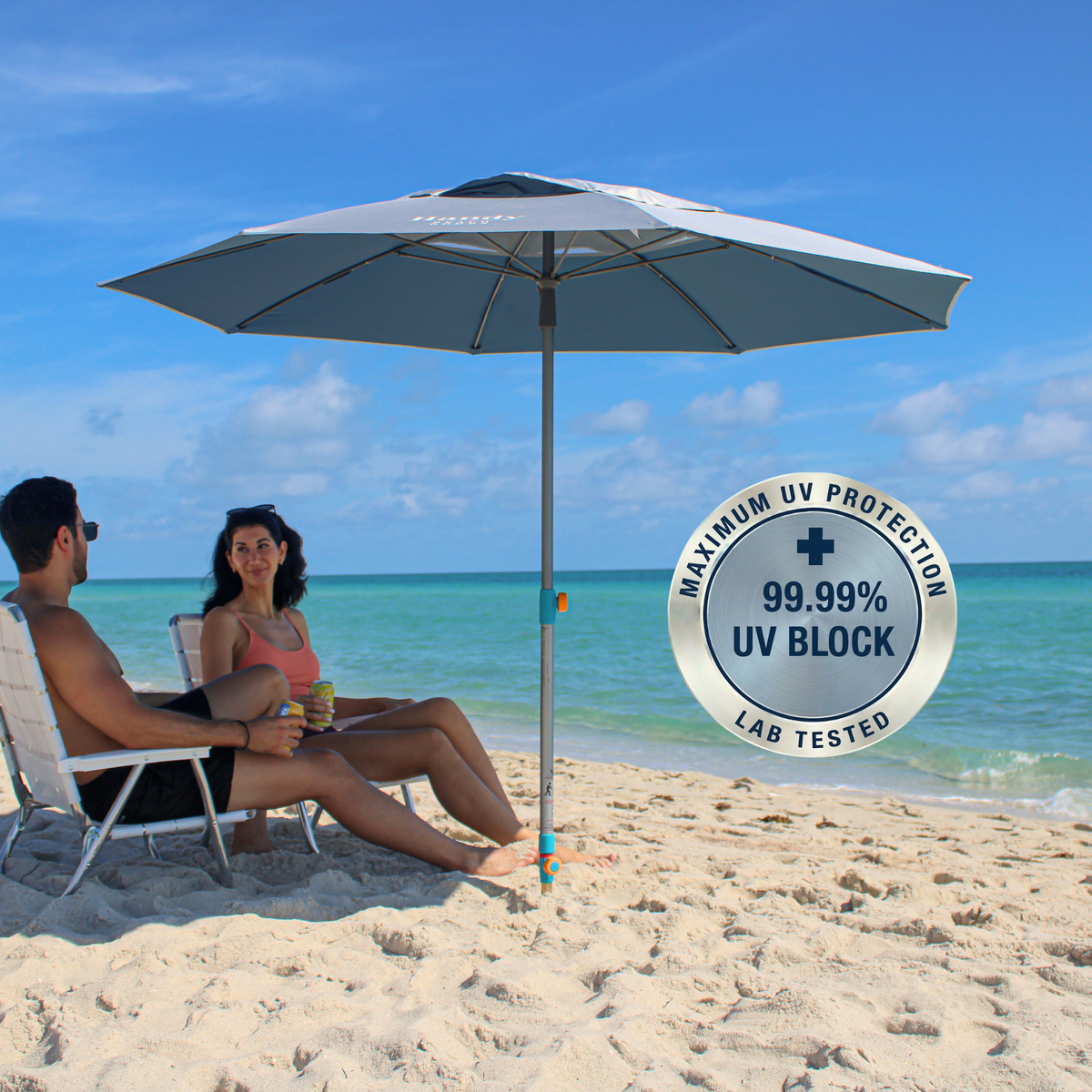 A silver beach umbrella with hammer-in anchor shading two people sitting in white lounge chairs under a blue sky. A circular badge on the right reads 'MAXIMUM UV PROTECTION"