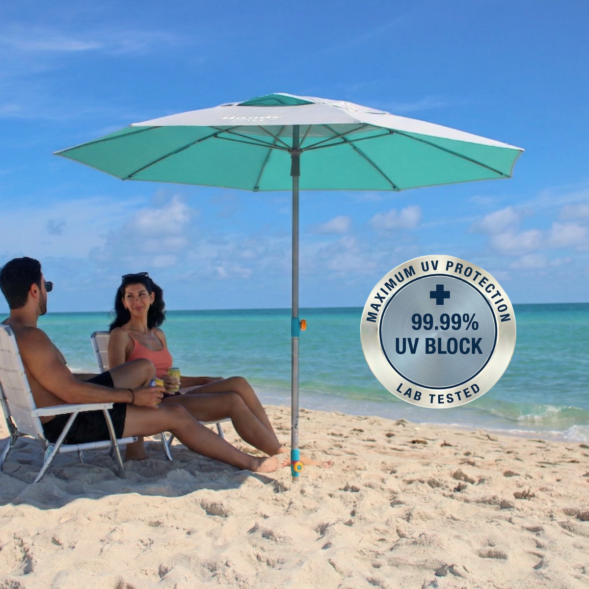 A silver top beach umbrella with a hemmer-in anchor shading two people sitting in lounge chairs. A circular badge on the right reads 'MAXIMUM UV PROTECTION"