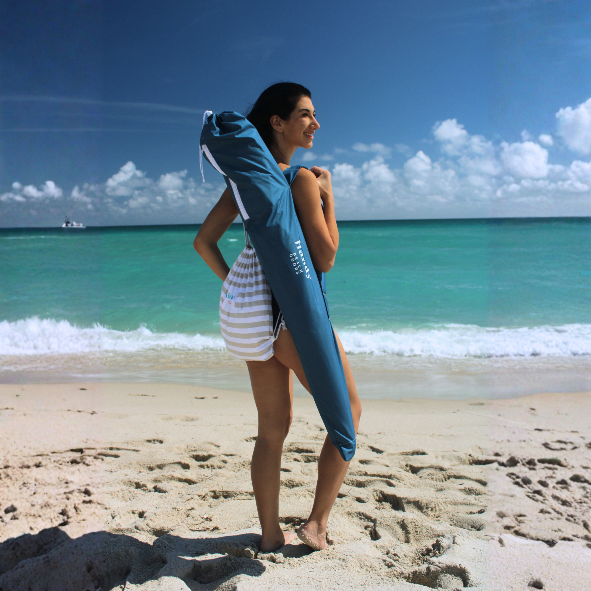 Woman holding a blue umbrella bag on a beach.