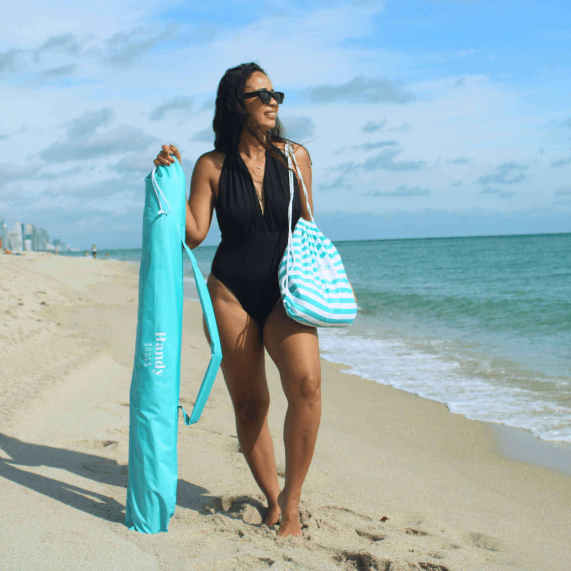 Woman on a beach holding a top-rated beach umbrella in a bag. teal umbrella system