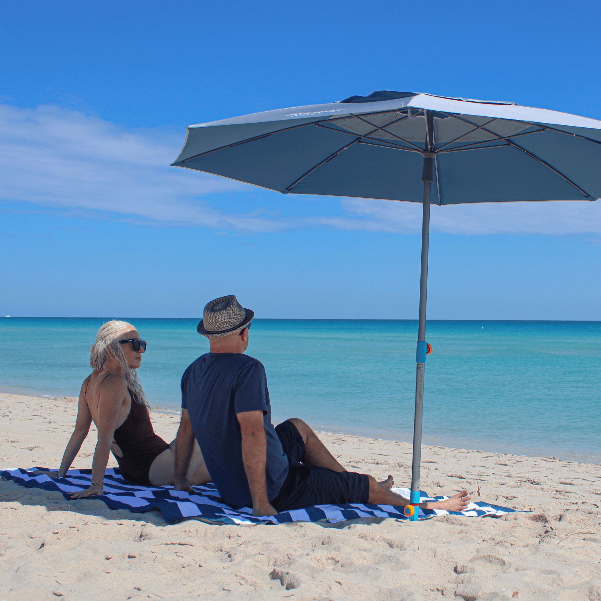 Couple relaxing by the ocean on a large waterproof beach blanket with an umbrella hole.