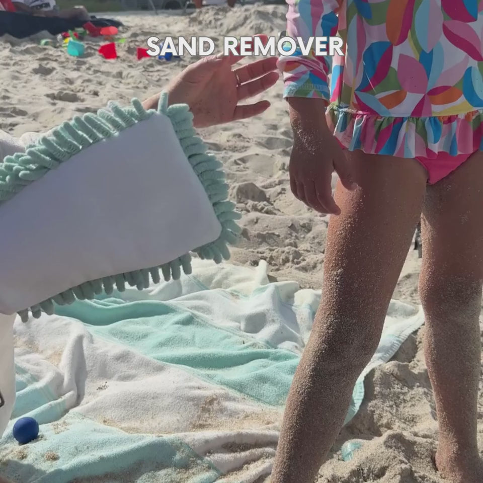 Parent using the blue chenille side of the Handy sand remover glove to effortlessly brush wet sand off a child's leg at the beach.