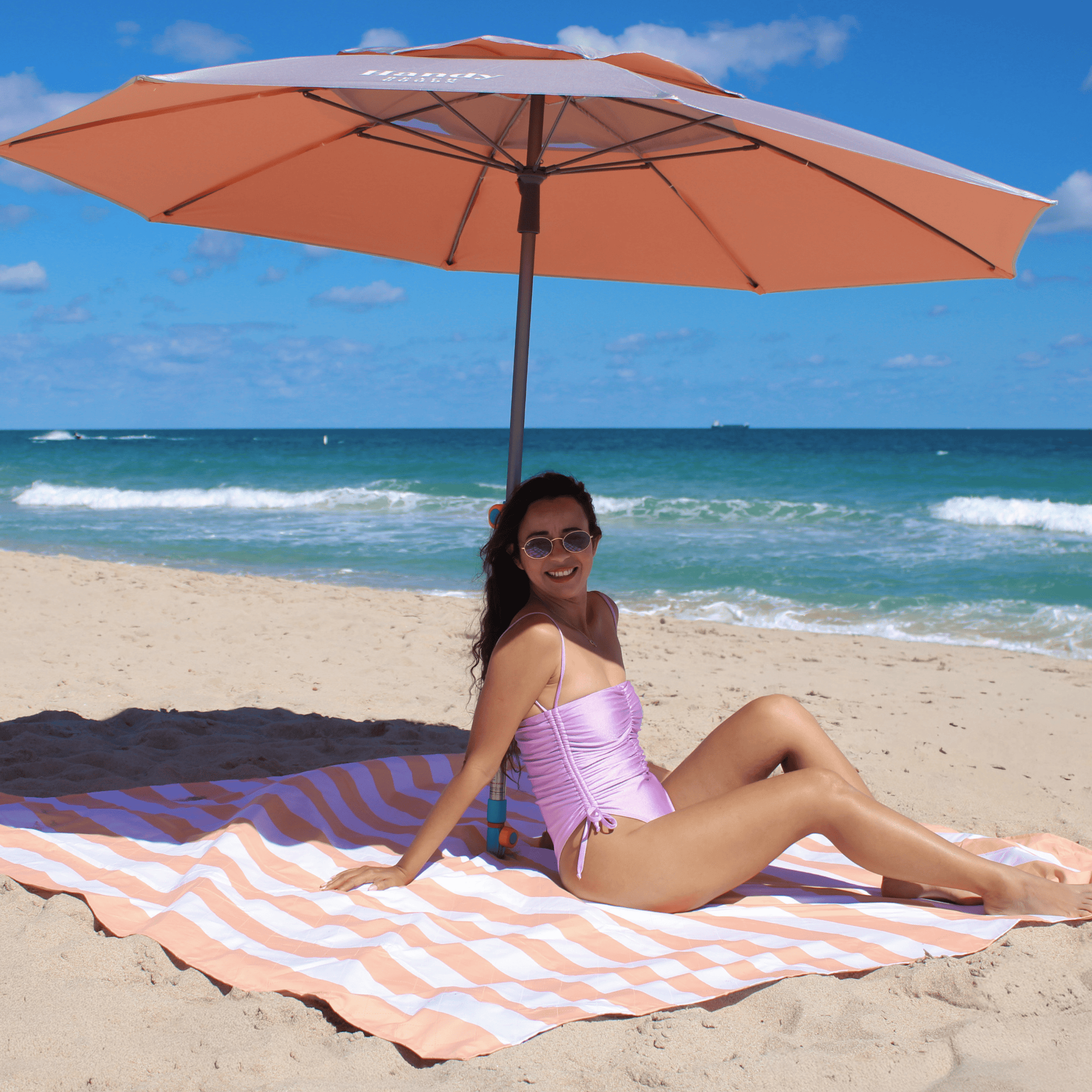 Silver and peach Handy Beach Umbrella providing deep shade for a woman relaxing on the beach. peach umbrella system 